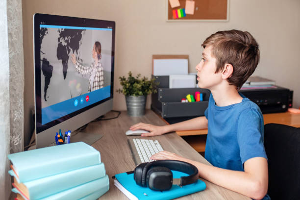 boy video conferences with a tutor on the computer at home. the concept of distance learning. the boy watches the lesson online and does homework remotely via the internet. - teacher back to school imagens e fotografias de stock