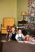 Two little boys sitting by Christmas tree and gifts. Iowa, USA, 1953. Kodachrome scanned film with grain.