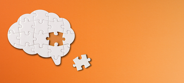 Brain shaped white jigsaw puzzle with copy space on orange background, a missing piece of the brain puzzle, mental health and problems with memory