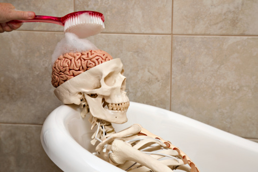 A close up shot of a skeleton laying in a bath tub and a brain in it's skull being scrubbed, concept shot for brainwashing or indoctrination.