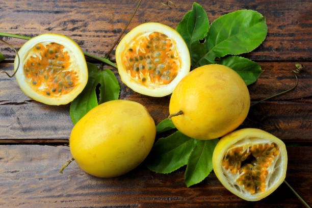 branches and leaves with yellow passion fruit and passion fruit cut in half isolated on wooden table. top view closeup - granadilla imagens e fotografias de stock
