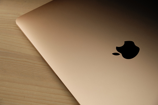 Recanati, Macerata, Italia - June 11, 2020: Brand new rose gold macbook air (2020) on a wooden table with the Apple logo highlighted in black, close up.