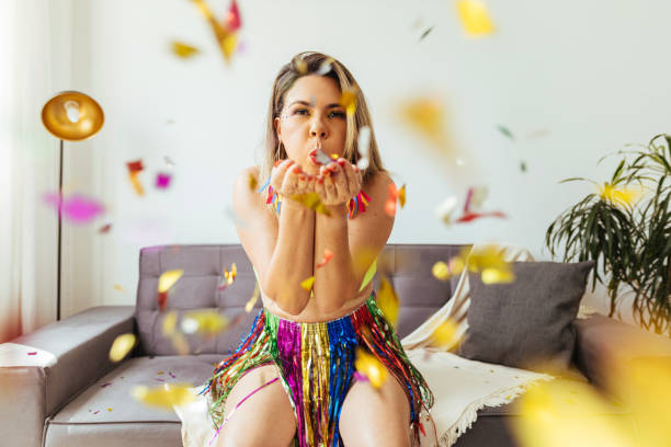 carnevale brasiliano. giovane donna che si gode il carnevale a casa soffiando coriandoli - carnevale foto e immagini stock