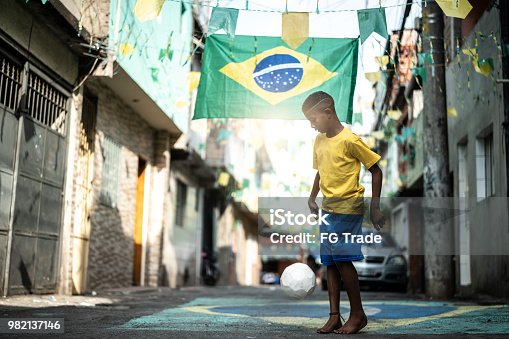 istock Brazilian Kid Playing Soccer in the Street 982137146