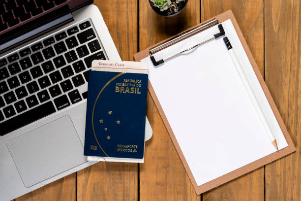 Brazilian passport and pass ticket on computer on wooden table. Blank notepad for travel planning stock photo