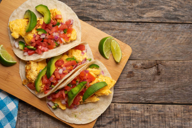 Breakfast egg tacos with flour tortilla and fresh sauce on wooden background stock photo