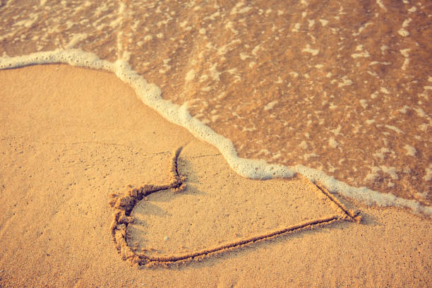 Breakup and divorce Heart drawn on the beach sand being washed away by a wave. Sand tone. Love affair, summer love or breakup and divorce concept. Ephemeral romantic love. Not true love. End of relationship. divorce beach stock pictures, royalty-free photos & images