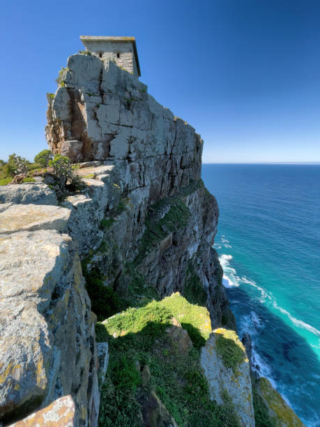 A breathtaking view of a structure on top of a sheer cliff cutting into the blue sea. stock photo