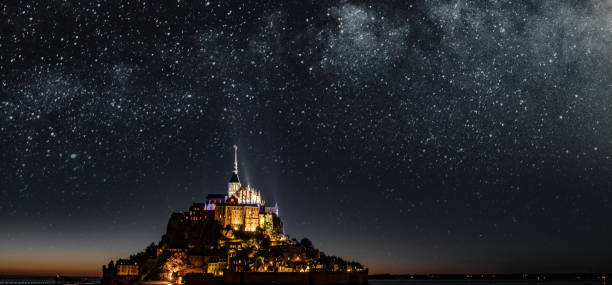 Breathtaking View of Mont-Saint-Michel, France, and the Milky Way Le Mont-Saint-Michel – Saint Michael's Mount is a tidal island and mainland commune in Normandy, France. Mont Saint-Michel and its bay are on the UNESCO list of World Heritage Sites. It is visited by more than 3 million people each year. Over 60 buildings within the commune are protected in France as monuments historiques. 

The presence of the community attracts many visitors and pilgrims who come to join in the various liturgical celebrations.

Due to its status as a popular place for pilgrimage, is completely freely accessible without any entrance fees or restrictions. pilgrims monument stock pictures, royalty-free photos & images