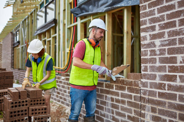 Bricklayer cementing bricks with trainee at site Bricklayer cementing bricks while trainee assisting him at site. They are in reflective clothing. Male and female workers are working at construction site. bricklayer stock pictures, royalty-free photos & images