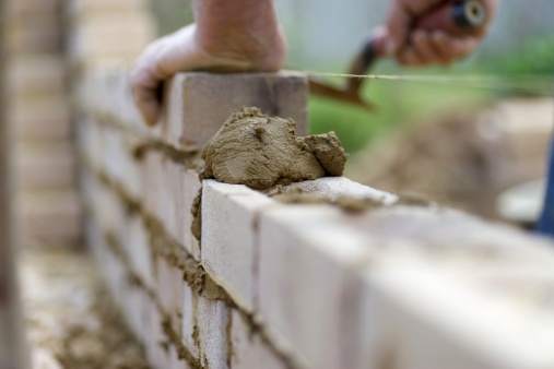 The experienced hands of a bricklayer as he lays the next course of bricks...