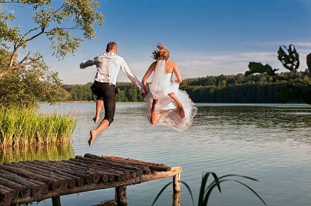 Bride and groom jumping in the lake. stock photo