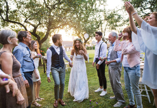 Bride, groom and guests at wedding reception outside in the backyard. Bride, groom and their guests at the wedding reception outside in the backyard. Family celebration. wedding guest dress stock pictures, royalty-free photos & images