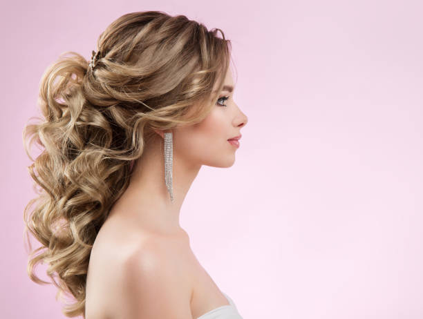 Bride Hairstyle and Make up. Woman Bridal Pinned Hair Curls. Model with Low Ponytail Evening Hairdo over Pink Background. Elegant Lady Profile with Glamour Curly Waves stock photo