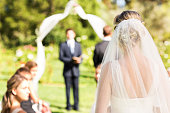 Rear view of bride wearing veil walking down the aisle during garden wedding. Horizontal shot.