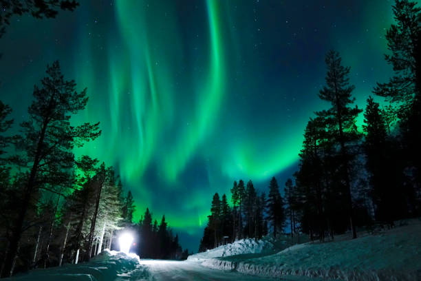 Bright lamp shining on the empty snowy road just as the northern lights appear. stock photo