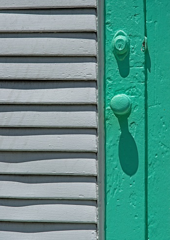 Bright light and shadow interplay on a bright turquoise colored louvered door in Key West Florida. The art deco style shape and colors can be used in other design elements and backgrounds.