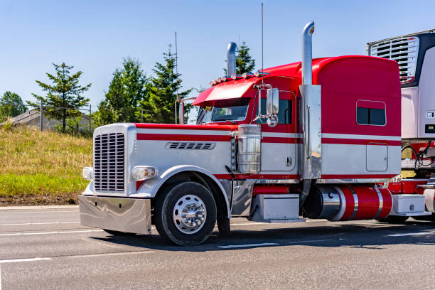 Bright two colors red and white big rig classic American semi truck transporting frozen cargo in refrigerator semi trailer running on the highway road with trees on the hillside stock photo