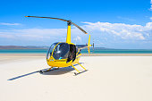 istock Bright yellow and black helicopter on the white sandy beach with blue ocean water behind it 1322088794