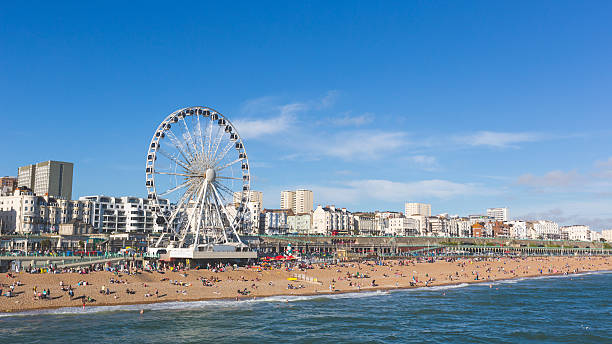 Brighton view of seaside from the pier Brighton view of seaside from the pier. Panoramic shot with the famous ferris wheel, the stones beach with unrecognizable persons on a sunny summer day. brighton stock pictures, royalty-free photos & images