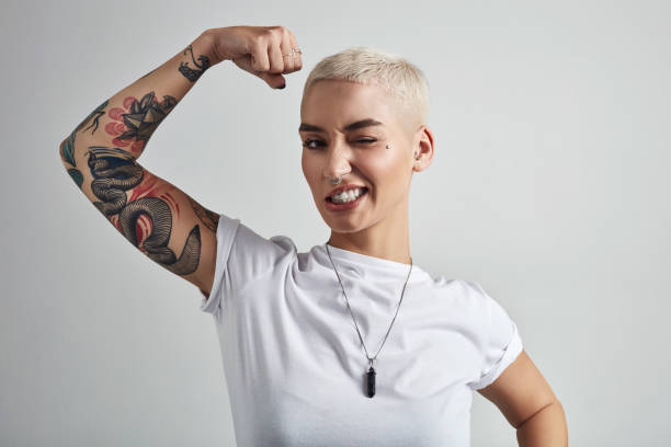 Bringing out the big guns Shot of an attractive young woman flexing her biceps against a grey background tattoo stock pictures, royalty-free photos & images