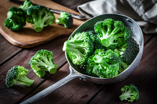 Fresh organic broccoli in an old metal colander shot on rustic wooden table. This vegetable is considered a healthy salad ingredient. Predominant colors are green and brown. Low key DSRL studio photo taken with Canon EOS 5D Mk II and Canon EF 100mm f/2.8L Macro IS USM