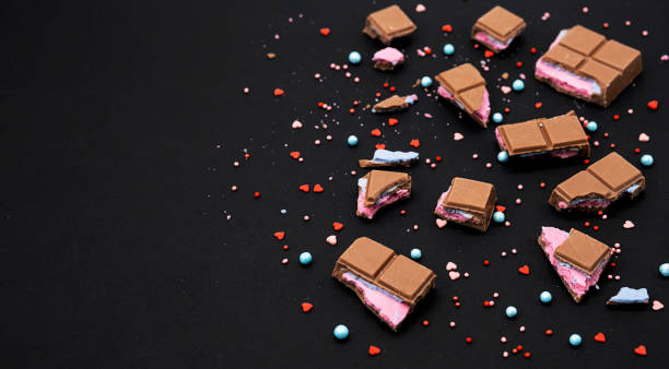 Broken pieces chocolate bar on black. Crumbled chocolate bar with pink blue filling of various size pieces, close up. Broken pieces chocolate bar on black. Crumbled chocolate bar with pink blue filling of various size pieces, close up. games like candy crush stock pictures, royalty-free photos & images