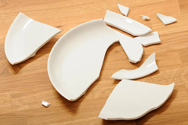 a broken white ceramic plate on a wooden floor - breekbaar bord stockfoto's en -beelden