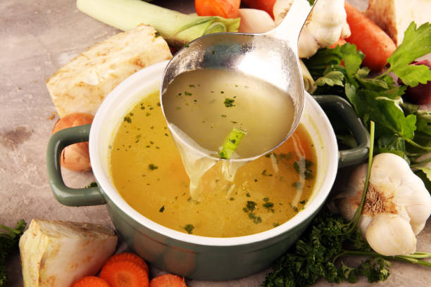 Broth with carrots, onions various fresh vegetables in a pot - colorful fresh clear spring soup. Rural kitchen scenery vegetarian bouillon stock stock photo