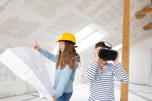 Brother and sister are on the construction site of their new room loft apartment with plan and yellow helmet and virtual reality goggles stock photo