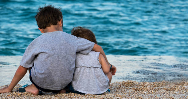 Brother and sister are sitting on the seashore embracing. Brother and sister are sitting on the seashore embracing. The boy carefully hugs the girl. The view from the back. Concept for Children's Day with place for text. tunisian girls stock pictures, royalty-free photos & images