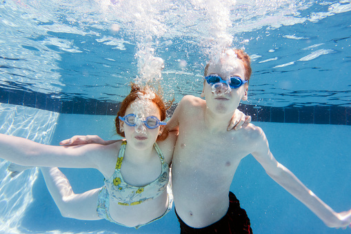 Brother and sister swimming underwater in swimming pool 