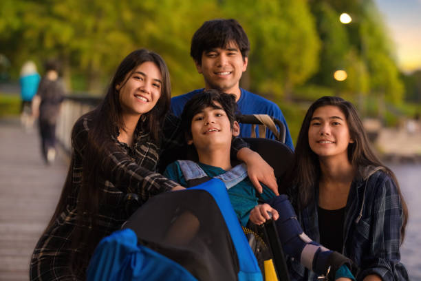 Brother and sisters surrounding disabled boy in wheelchair at park stock photo