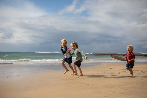 Brothers running on a beach next to the water stock photo