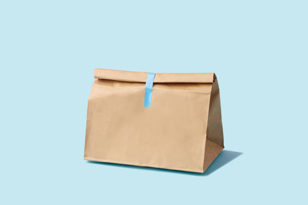 Brown clear empty blank paper bag for food delivery on blue background with copy space. Packaging template mock up fast food. Brown clear empty blank paper bag for food delivery on blue background with copy space. Packaging template mock up fast food. take out food stock pictures, royalty-free photos & images
