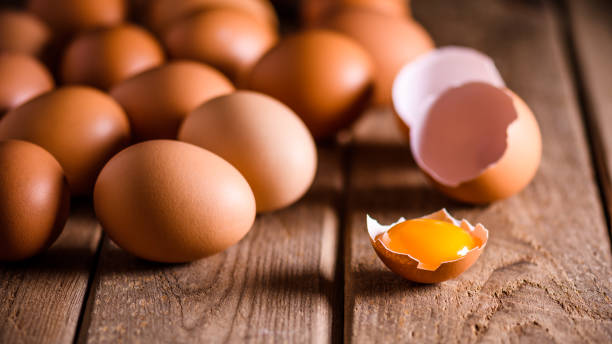 Brown eggs on wooden table with one broken and egg yolk on the eye, with space for text stock photo