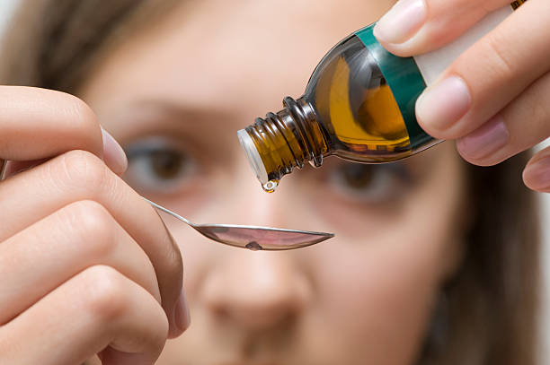Brown eyed woman trying to correctly dose an herbal medicine Dripping herbal essence of a vial over a spoon homeopathic medicine stock pictures, royalty-free photos & images