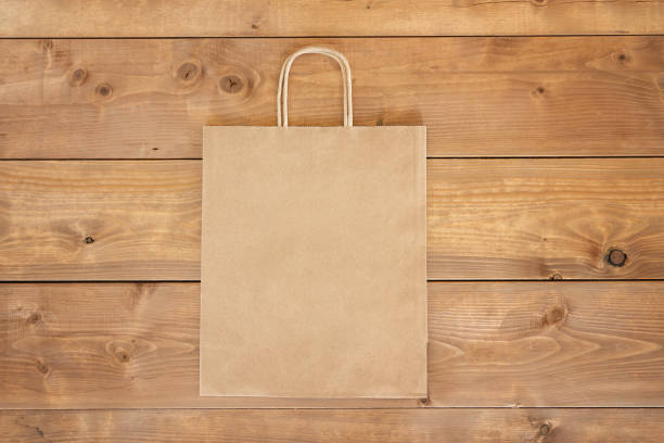 Brown paper craft bag on wooden background. Centre composition with empty spot for text. Responsive design mockup. Flat lay stock photo