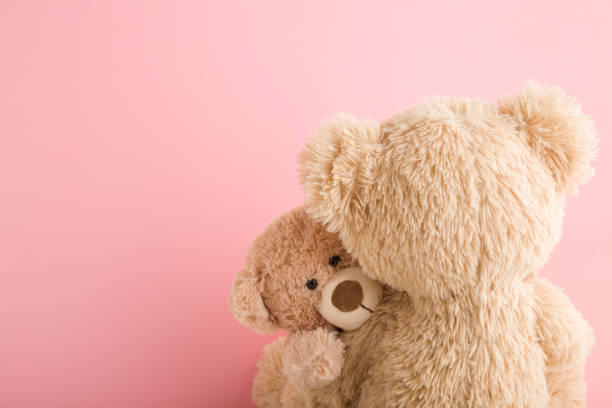 Brown teddy bear mother hugging her baby on light pink background. Lovely, emotional moment. Closeup. Copy space. Empty place for emotional text, cute quote or sayings. stock photo