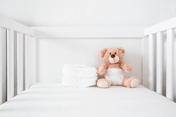 bruine teddybeer met witte luier zittend in baby bed. - cradle to cradle stockfoto's en -beelden
