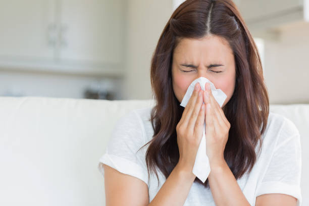 Brunette sneezing in a tissue stock photo