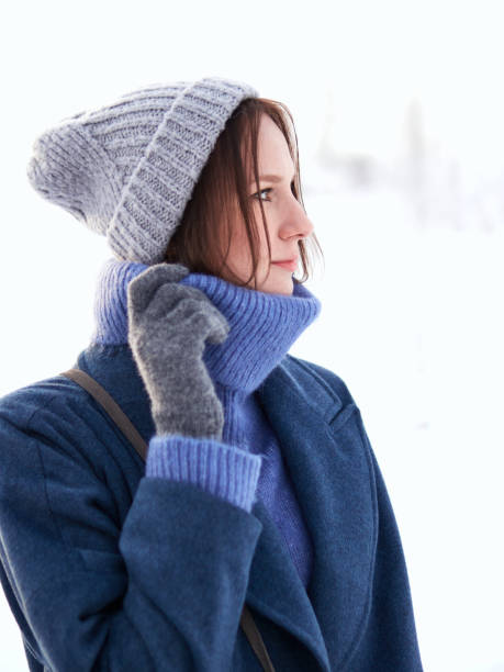 brunette walks through the winter forest in a gray hat, blue sweater and blue coat stock photo
