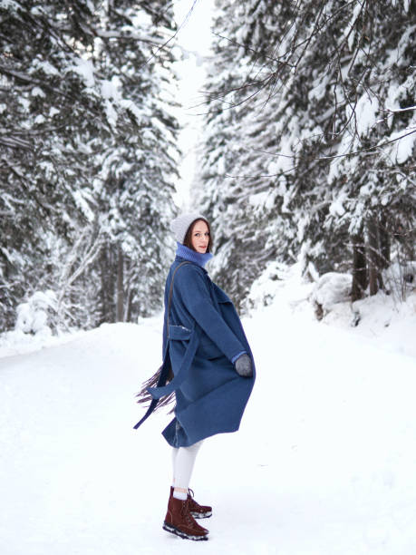 brunette walks through the winter forest in a gray hat, blue sweater and blue coat stock photo