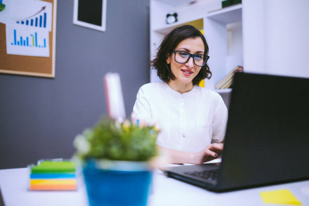 Brunette Woman In Eyeglasses Typing Report Brunette Woman In Eyeglasses Typing Morning Report At Her Desk At The Office bureaucracy stock pictures, royalty-free photos & images