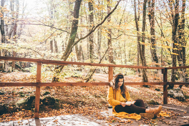 brunette woman in yellow sweater sitting on a fallen autumn leaves in a park, reading a book or write a diary - write down 個照片及圖片檔