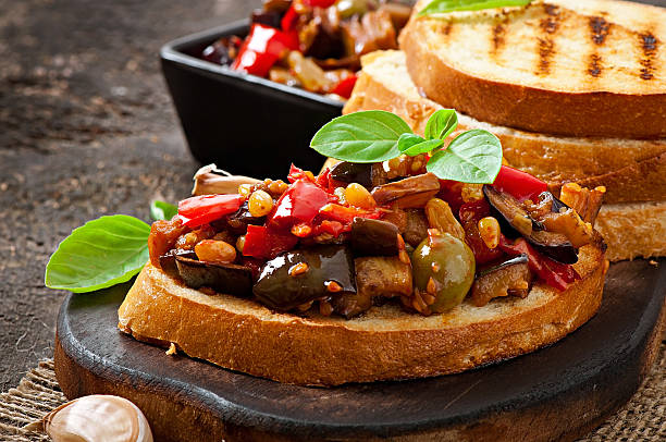 Bruschetta caponata with raisins and pine nuts Bruschetta caponata with raisins and pine nuts decorated with a leaf of basil crostini photos stock pictures, royalty-free photos & images