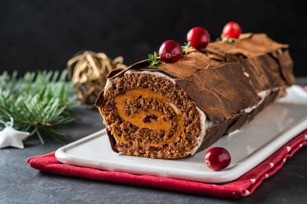 Buche de Noel. Traditional Christmas dessert, Christmas yule log cake with chocolate cream, cranberry. On stone gray background with Christmas tree branches. stock photo