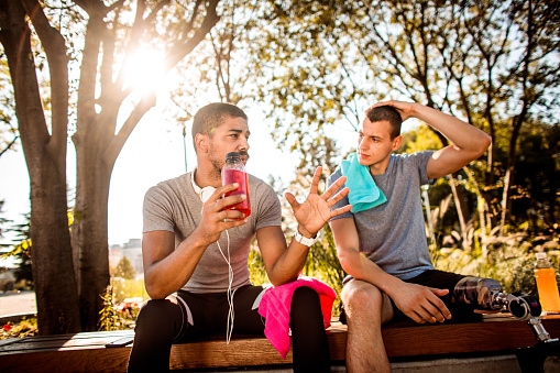 Buddies Talking And Resting After Jogging Session On A Park Bench