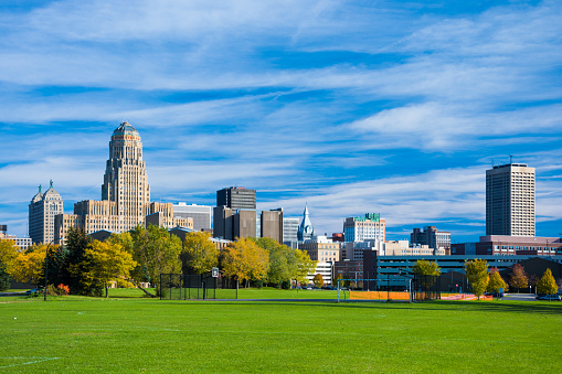Downtown Buffalo skyline from a park during Autumn, with many clouds in the sky.  The building to the left is Buffalo City Hall.