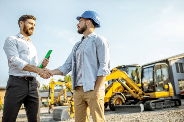 Builder with a sales consultant at the shop with heavy machinery Builder choosing heavy machinery for construction with a sales consultant standing with some documents on the open ground of a shop with special vehicles construction equipment stock pictures, royalty-free photos & images